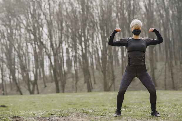 athletic sportswoman performing front double biceps pose in park